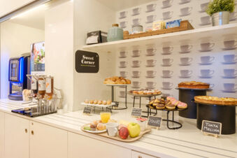 Counter at B&B Hotel Ravenna with various pastries including croissants, muffins, donuts, fruit, juice, and a coffee machine