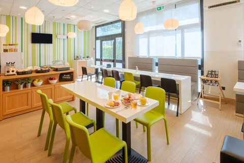 Dining area with green chairs and white tables set with breakfast plates inside B&B Hotel Ravenna