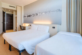 B&B Hotel Ravenna guest room with two white beds, a desk and chair, wooden floor, wall mural, and dark wooden door
