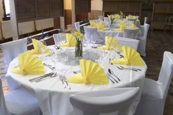 Sl&aacute;vnostne prestret&eacute; stoly so žlt&yacute;mi obr&uacute;skami a kvetinovou v&yacute;zdobou v re&scaron;taur&aacute;cii hotela Gasthaus Zur Linde Diersburg.