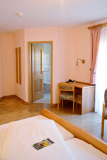 Hotel Gasthaus Zur Linde Diersburg room with bed, wooden desk and chair, open bathroom door, tiled floor, and pink curtains