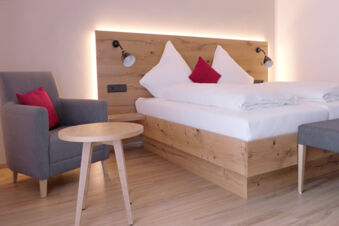 Hotel Gasthaus Zur Linde Diersburg room with wooden bed frame, white bedding, gray armchair with red cushion, and wooden table