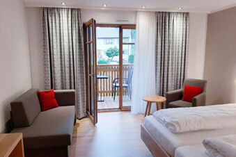 Hotel Gasthaus Zur Linde Diersburg room with bed, brown sofa and chair with red cushions, wooden side table, and balcony door open