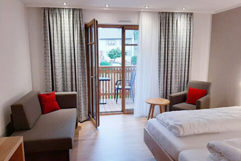 Hotel Gasthaus Zur Linde Diersburg room with bed, brown sofa and chair with red cushions, wooden side table, and balcony door open