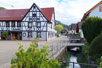 Traditional half-timbered building of Hotel Gasthaus Zur Linde Diersburg with flowers along a small stream in the village