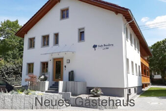 White multi-story building with wooden-framed windows, small landscaped garden, and sign Hotel Gasthaus Zur Linde Diersburg