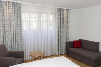 Svetl&aacute; izba pre host&iacute; v hoteli Gasthaus Zur Linde Diersburg s pohovkou, kreslom, dreven&yacute;m stolom a veľk&yacute;mi oknami so z&aacute;vesmi.