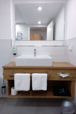 A wooden bathroom vanity with a white rectangular sink, mirror, two towels, and accessories at Hotel Gasthaus Zur Linde Diersburg