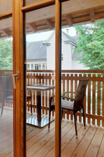 View through glass door to a wooden balcony with two black chairs and a table at Hotel Gasthaus Zur Linde Diersburg surrounded by trees