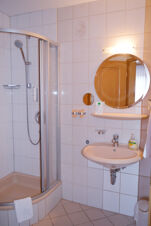 Bathroom with shower, round mirror, sink, soap dispenser, and towel at Hotel Gasthaus Zur Linde Diersburg