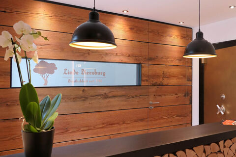 Modern&aacute; recepcia s dreven&yacute;m obložen&iacute;m, čiernym pultom a z&aacute;vesn&yacute;mi svetlami v hoteli Gasthaus Zur Linde Diersburg, pr&iacute;jemn&aacute; atmosf&eacute;ra.