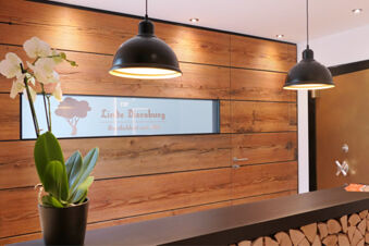 Reception area of Hotel Gasthaus Zur Linde Diersburg with wooden walls, a black lamp, and a potted orchid on the counter