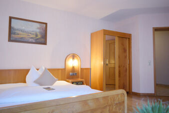 Simple guest room with wooden bed, bedside table, lit wall lamp, wardrobe, and a landscape painting at Hotel Gasthaus Zur Linde Diersburg