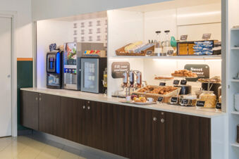 Breakfast buffet setup with croissants, jars of cereal and jams, coffee machines, and packaged snacks at B&B Hotel Faenza