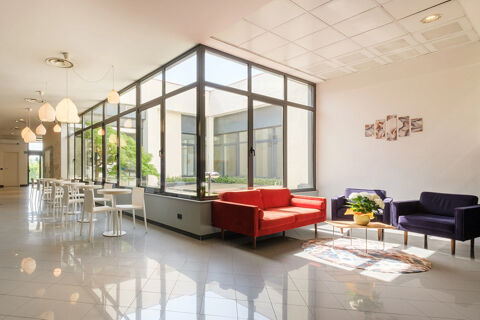 Bright seating area at B&B Hotel Faenza featuring red and purple sofas, a wooden coffee table, and white dining tables with chairs