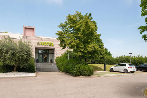 Entrance of B&B Hotel Faenza showing steps, greenery, parked cars, and the hotel building under a clear sky