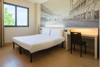 Minimalist hotel room at B&B Hotel Faenza with a double bed, a desk with a chair, and a large black and white wall mural