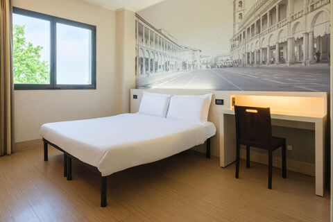 Minimalist hotel room at B&B Hotel Faenza with a double bed, a desk with a chair, and a large black and white wall mural