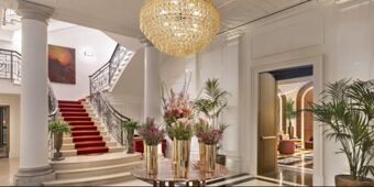 Elegant hotel interior of InterContinental Rome Ambasciatori Palace with grand staircase, chandelier, floral arrangements, and potted plants