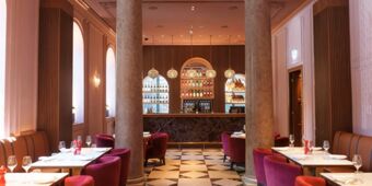 Dining area at InterContinental Rome Ambasciatori Palace with a marble floor, columns, red chairs, and a bar with bottles on shelves