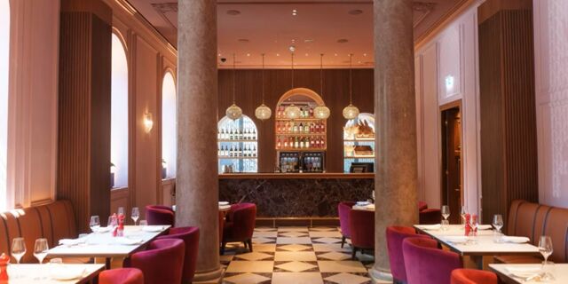 Dining area at InterContinental Rome Ambasciatori Palace with a marble floor, columns, red chairs, and a bar with bottles on shelves