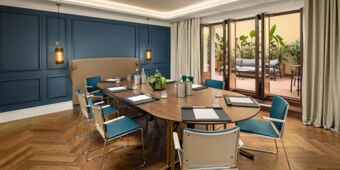 Meeting room at InterContinental Rome Ambasciatori Palace with wooden table, blue chairs, pendant lights, and outdoor patio seating visible