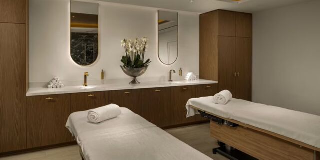Two massage tables with rolled towels in a room featuring wooden cabinets, sinks, mirrors, and a flower arrangement at InterContinental Rome Ambasciatori Palace