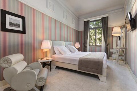 Bedroom in Grand Hotel Palace with a double bed, two bedside lamps, armchair, window with curtains, and wall-mounted TV