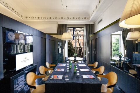 Modern meeting room at Grand Hotel Palace with wooden chairs, black table, bottled water, and city view window