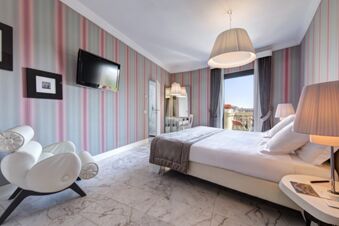 Bright hotel room at Grand Hotel Palace with a double bed, striped wallpaper, a chair, TV, lamps, and balcony view