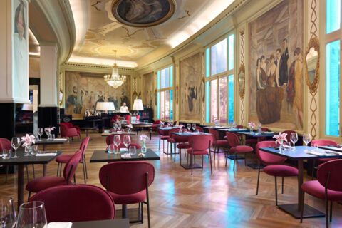 Dining area at Grand Hotel Palace featuring red chairs, black tables with glassware and floral centerpieces, large windows and murals