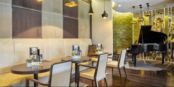Seating area with tables, chairs, a beige bench, and a black grand piano against a mirrored wall at Crowne Plaza Rome -St. Peter's
