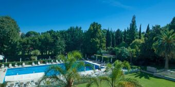 Outdoor swimming pool surrounded by lounge chairs and tall trees at Crowne Plaza Rome -St. Peter's under clear blue sky