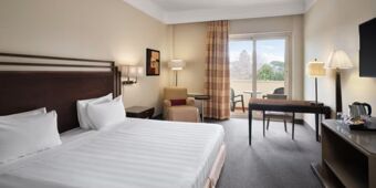 Hotel room at Crowne Plaza Rome -St. Peter's with a large bed, armchair, desk, lamps, and balcony with outdoor seating