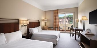 Hotel room at Crowne Plaza Rome -St. Peter's with two double beds, bedside lamps, a desk, chair, balcony and wall-mounted TV