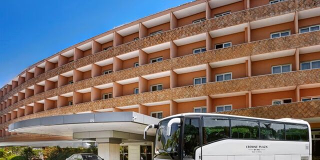 Curved multi-story building facade with balconies and a Crowne Plaza Rome -St. Peter's shuttle bus parked in front