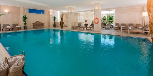 Indoor swimming pool at Crowne Plaza Rome -St. Peter's with lounge chairs, potted plants, towels, and a lifebuoy on the wall