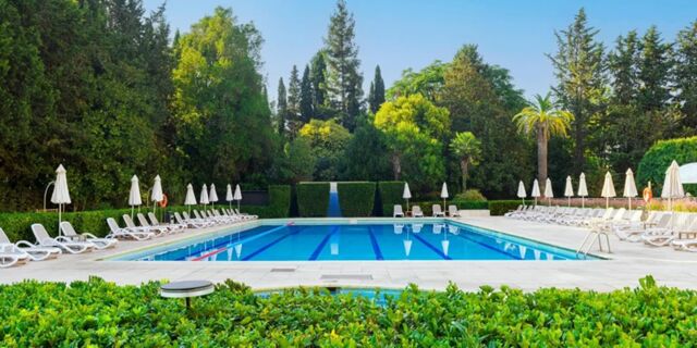 Outdoor swimming pool at Crowne Plaza Rome - St. Peter's surrounded by white lounge chairs, umbrellas, and dense green trees