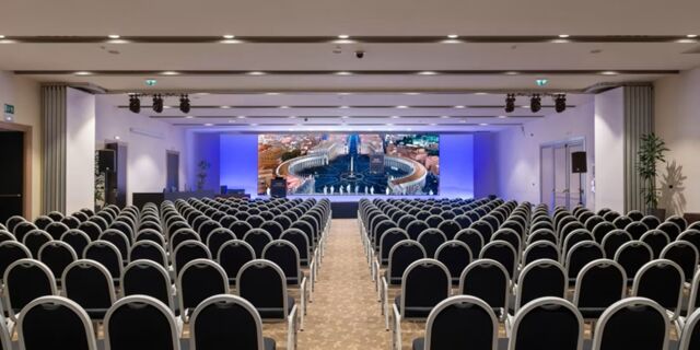 Conference room at Crowne Plaza Rome -St. Peter's with rows of black chairs facing a large screen showing an aerial city view