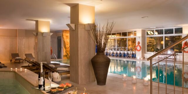Indoor pool area at Crowne Plaza Rome -St. Peter's with lounge chairs, a large vase, candles, and snacks on a table near the water