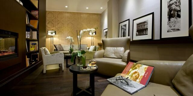Cozy lounge area at Crowne Plaza Rome -St. Peter's with beige armchairs, a book on a couch, round tables, and framed photos on walls