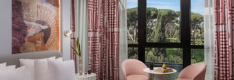 Hotel nhow Roma Vittorio Veneto room with white pillows, pink chairs, small table with books, and large window view of trees