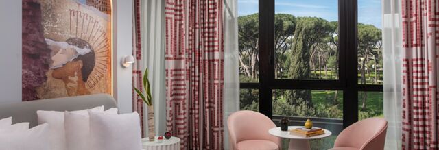 Hotel nhow Roma Vittorio Veneto room with white pillows, pink chairs, small table with books, and large window view of trees