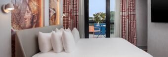 Hotel nhow Roma Vittorio Veneto room with white bed and pillows, patterned curtains, wall art, balcony table and chairs with plants visible outside