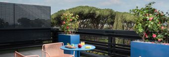 Balcony seating area at Hotel nhow Roma Vittorio Veneto with a round blue table, two chairs, plants, and trees in the background