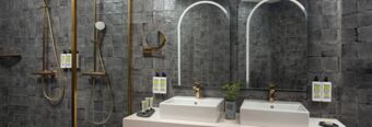 Modern bathroom with dual sinks, gold shower fixtures, grey tiled walls, mirrors, and toiletries at Hotel nhow Roma Vittorio Veneto