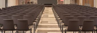 Empty meeting room with rows of brown chairs aligned facing a stage in Hotel nhow Roma Vittorio Veneto conference area