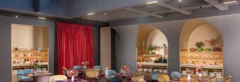 Dining area with colorful chairs and red curtains inside Hotel nhow Roma Vittorio Veneto featuring arched shelving with plants and dishes