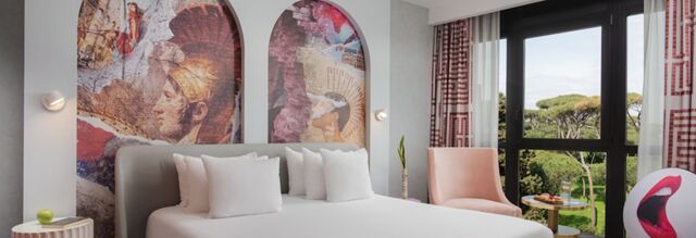 Hotel nhow Roma Vittorio Veneto bedroom with a large bed, artistic wall murals, a pink chair, and a view of trees through the window
