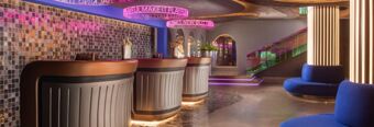 Reception area of Hotel nhow Roma Vittorio Veneto with curved desks, mosaic wall, neon signage, and blue seating areas